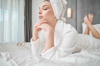 Bornozlu kadın evdeki yatakta yatıyor.