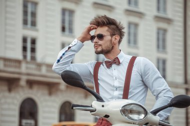 Sokakta klasik scooter kullanan çok şık bir adam, beyaz bir gömlek giyiyor.
