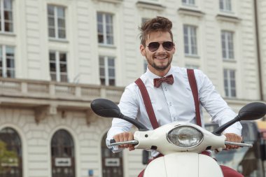 Sokakta klasik scooter kullanan çok şık bir adam, beyaz bir gömlek giyiyor.