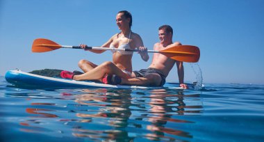 Genç ve güzel aşıklar açık okyanusta bir sörf tahtasının üzerinde oturuyorlar..