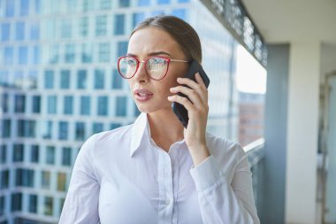 Modern ofis binasının yakınında cep telefonuyla konuşan kadın emlakçı.