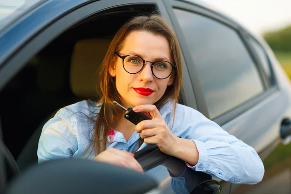 Νεαρή όμορφη γυναίκα που κάθεται σε ένα αυτοκίνητο με τα κλειδιά στο χέρι — Φωτογραφία Αρχείου