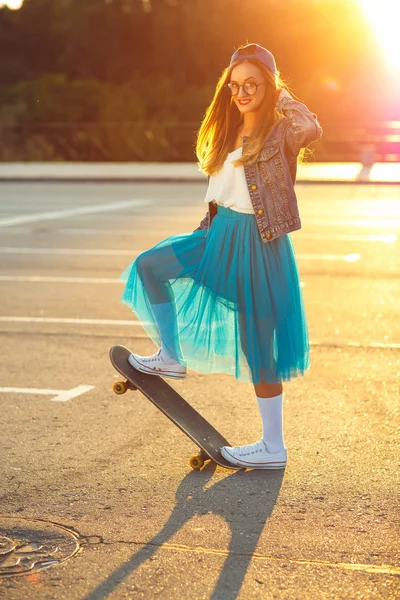 Schöne junge Frau mit Skateboard, bei Sonnenuntergang beleuchtet — Stockfoto