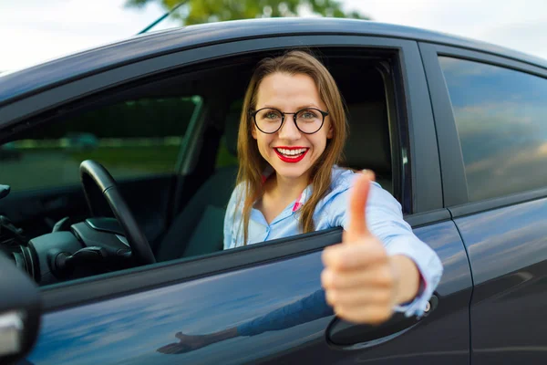 Mladá šťastná žena, sedící v autě s palcem — Stock fotografie