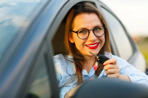 Joven mujer bonita sentada en un coche con las llaves en la mano — Foto de Stock