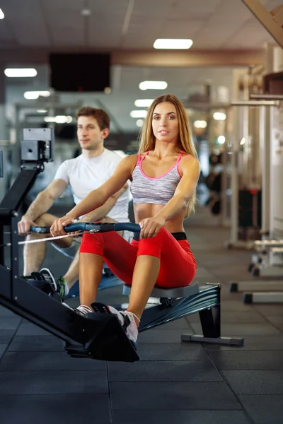 Athletic man and woman training on row machine in gym
