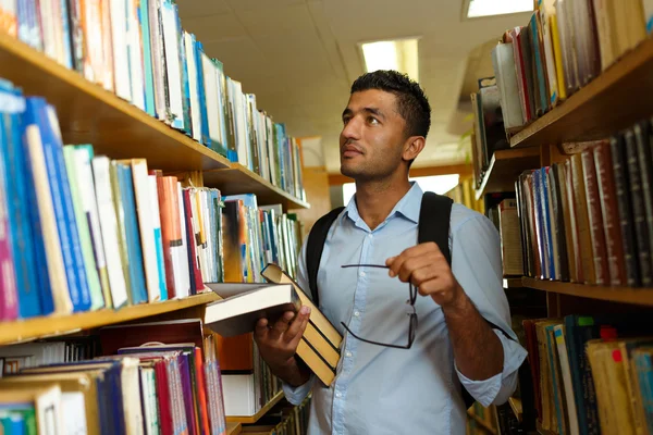 Student, čtení knihy mezi regály v knihovně — Stock fotografie