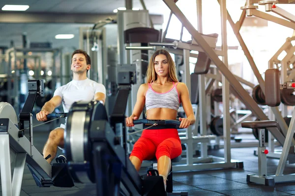 Allenamento atletico uomo e donna sulla macchina da fila in palestra — Foto Stock