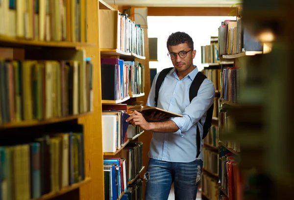 Student, czytanie książki między półkami w bibliotece — Zdjęcie stockowe