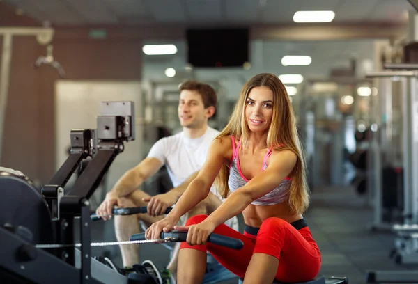 Hombre y mujer atléticos entrenando en la máquina de fila en el gimnasio — Foto de Stock