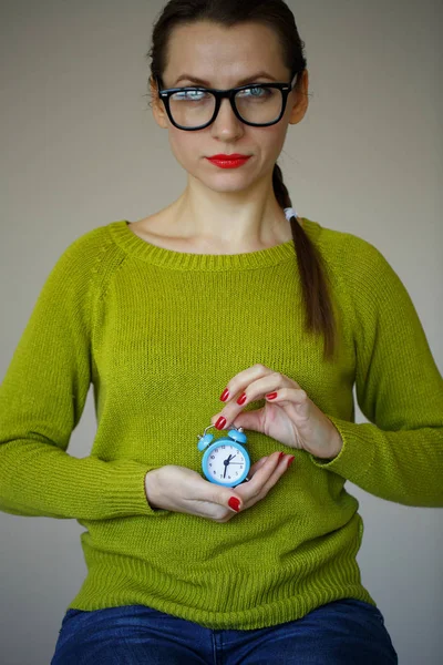 Pequeño despertador azul en las manos de una joven pensativa — Foto de Stock