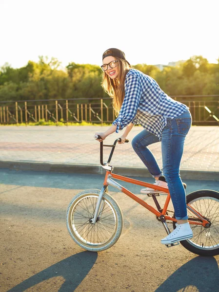 Schöne junge Frau mit Hut, die auf einem Fahrrad vor dem Hintergrund der Stadt fährt — Stockfoto