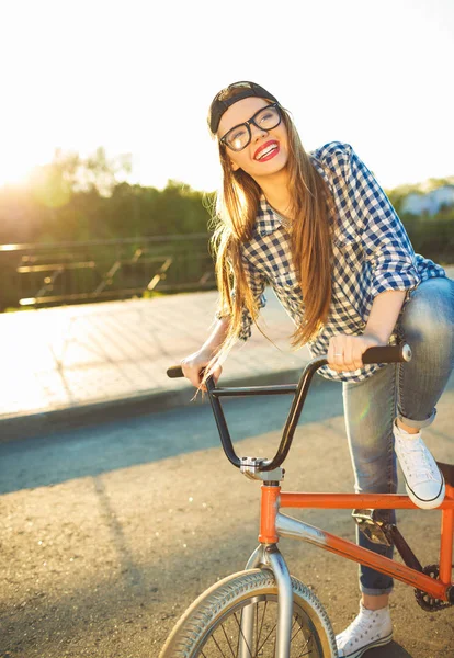 Preciosa mujer joven en un sombrero montando una bicicleta en el fondo de la ciudad — Foto de Stock