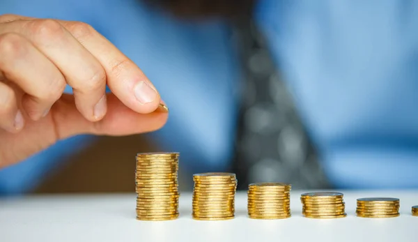 Male hand stacking gold coins into increasing columns — Stock Photo, Image