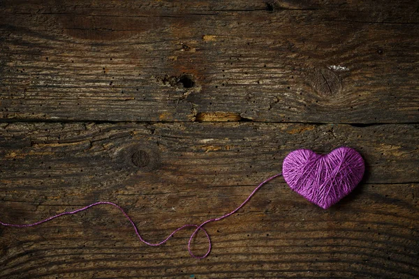 Coração roxo com uma bola de linha em no velho backg de madeira gasto — Fotografia de Stock