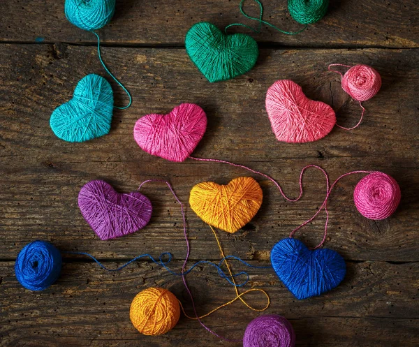 Corações multicoloridos com bolas de fio no velho fundo de madeira gasto — Fotografia de Stock