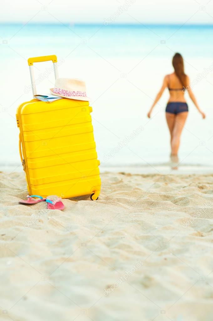 Yellow suitcase on the beach and a girl walks into the sea in th