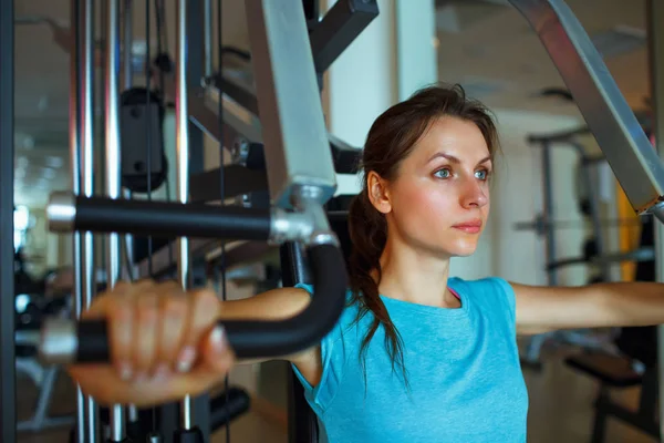 Mujer atlética trabaja en aparatos de entrenamiento en el gimnasio — Foto de Stock