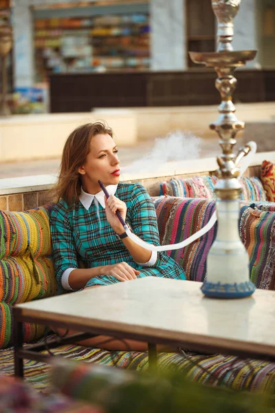 Beautiful young woman smokes a hookah in a cafe — Stock Photo, Image