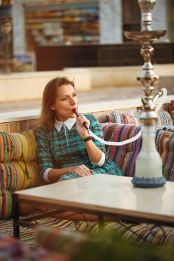 Güzel genç kadın bir kafede nargile sigara içiyor.