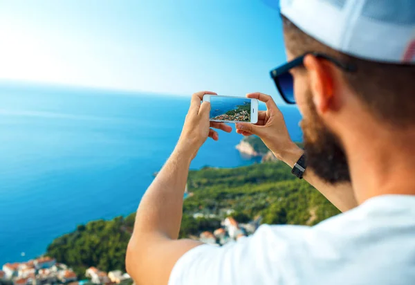 Homem faz fotos por um smartphone no fundo da costa do mar , — Fotografia de Stock