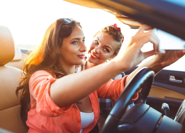 Duas meninas bonitas jovens estão fazendo selfie em um conversível — Fotografia de Stock