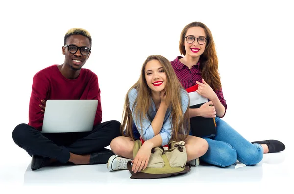Tres estudiantes felices sentados con libros, laptop y bolsas —  Fotos de Stock