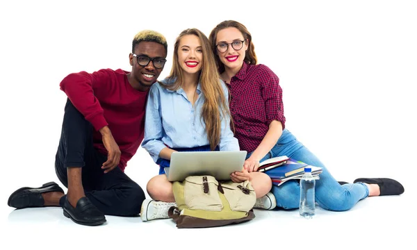 Três estudantes felizes sentados com livros, laptop e bolsas — Fotografia de Stock