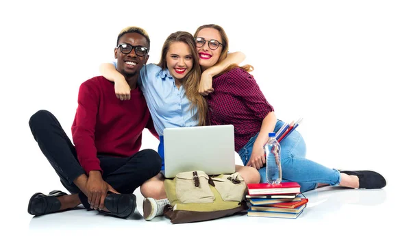 Three happy students sitting with books, laptop and bags — Stock Photo, Image