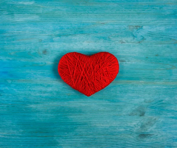 Red heart shape made from wool on blue wooden background — Stock Photo, Image