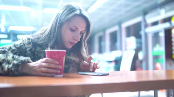 Woman using app on smartphone and drinking coffee in cafe — Stock Video