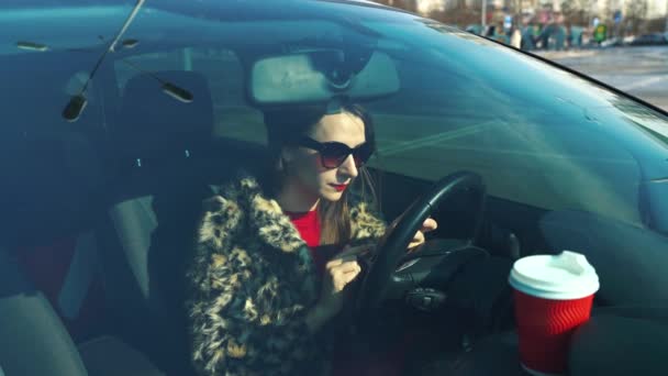 Vacker kvinna i päls med en smartphone och dricka kaffe i bilen — Stockvideo