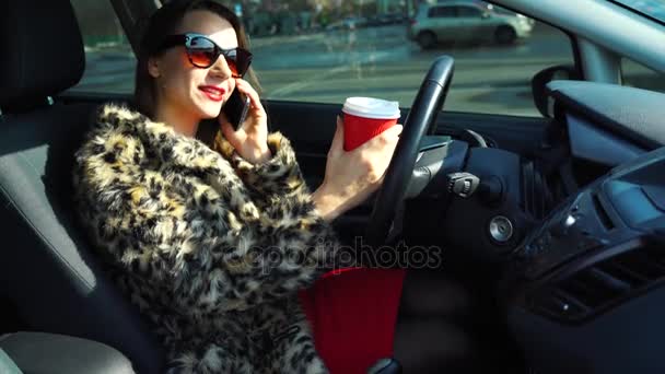 Schöne Frau im Pelzmantel mit Smartphone und Kaffee trinken im Auto — Stockvideo