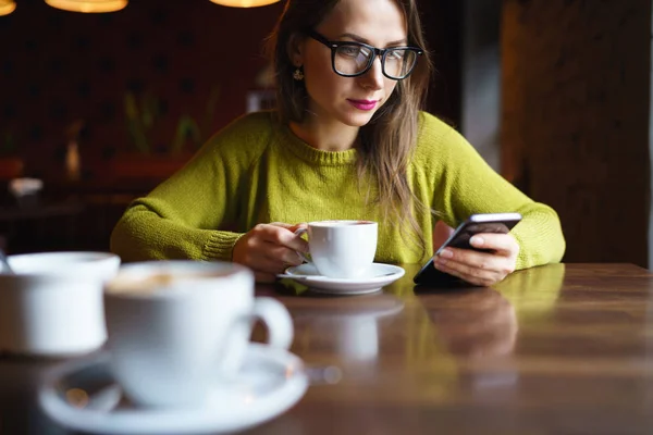 Giovane donna bere caffè e utilizzando smartphone in caffè — Foto Stock