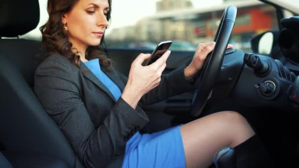 Vrouw in een blauwe jurk en jas met behulp van een smartphone in de auto — Stockvideo