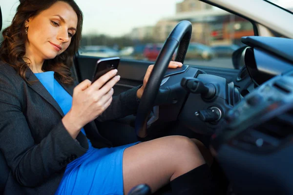 Wanita dalam gaun biru dan jaket menggunakan smartphone di dalam mobil — Stok Foto