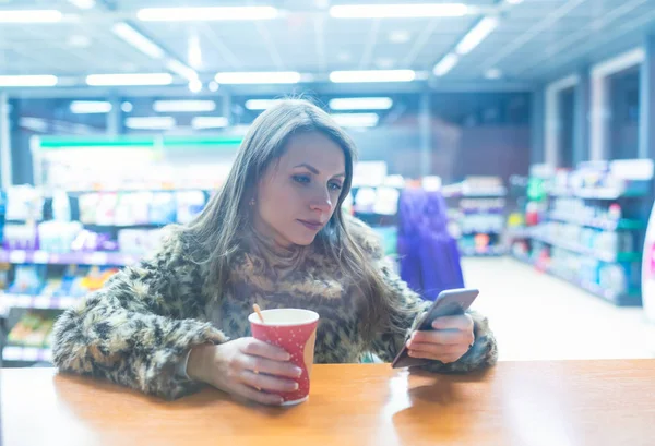 Mujer usando la aplicación en el teléfono inteligente y beber café en la cafetería — Foto de Stock