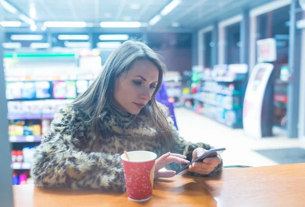 Mujer usando la aplicación en el teléfono inteligente y beber café en la cafetería — Foto de Stock