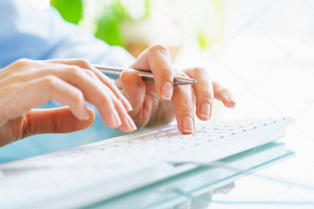 Woman office worker with pen in hand typing on the keyboard