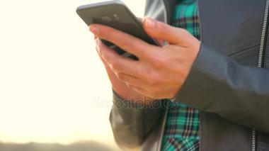 Kadın bir akıllı telefon açık havada günbatımında kullanıyor
