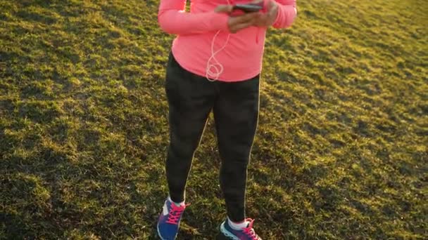 Mulher se preparando para uma corrida seleciona a música no smartphone no estádio ao pôr do sol — Vídeo de Stock