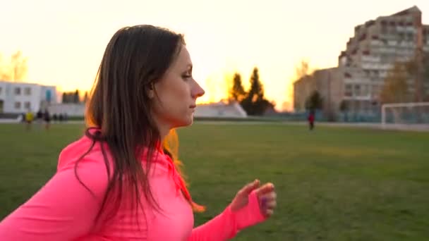 Γυναίκα τρέχει μέσα από το γήπεδο στο ηλιοβασίλεμα, αργή κίνηση — Αρχείο Βίντεο