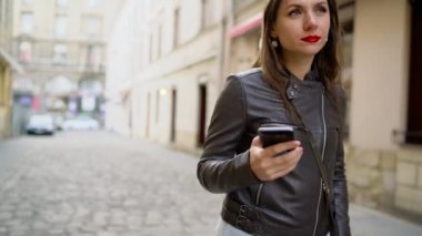 Kadın kırmızı dudaklar ile smartphone kullanır ve Ortaçağ cadde boyunca elini kolunu sallaya dönüyor