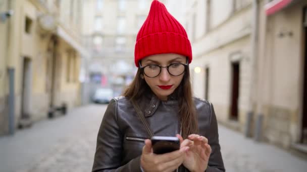 Mujer con labios rojos utiliza smartphone y paseos por la calle medieval — Vídeos de Stock