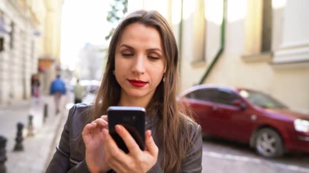 Woman with red lips uses smartphone and strolls along the medieval street — Stock Video