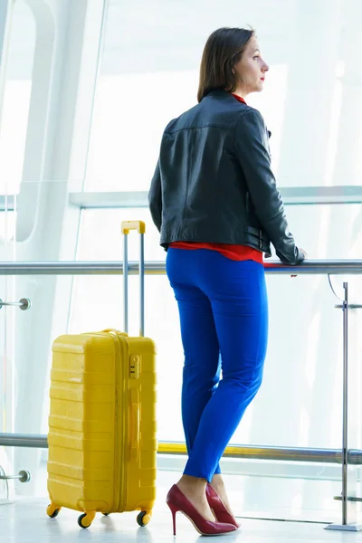 Mujer con ropa brillante y maleta amarilla en el airpo — Foto de Stock