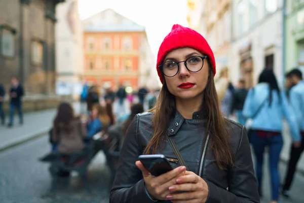 Kvinna med röda läppar och röd hatt använder smartphone och promenader alon — Stockfoto