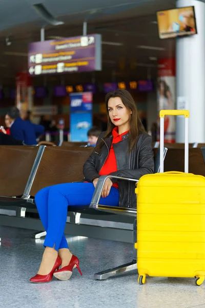 Donna in abiti luminosi con valigia gialla si siede in aeroporto — Foto Stock