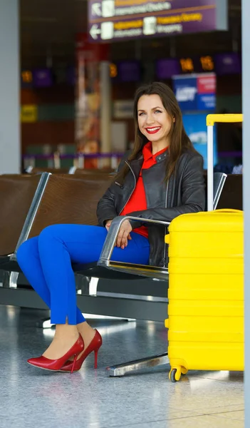 Woman in bright clothes with yellow suitcase sits at the airport — Stock Photo, Image