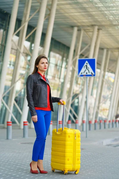 Mujer en ropa brillante con la maleta amarilla está de pie nea — Foto de Stock